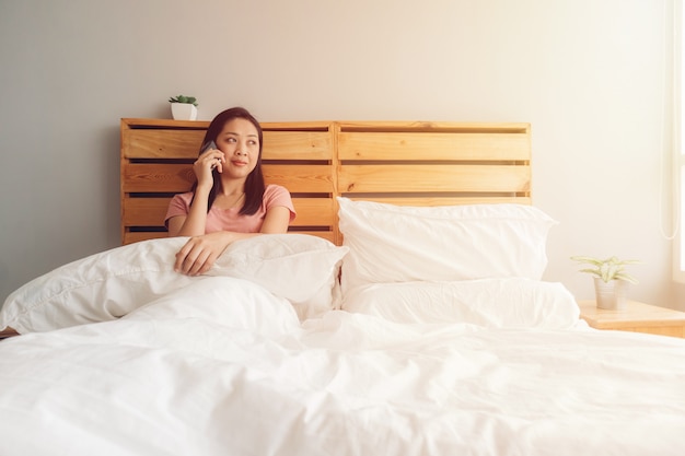 Woman is having a phone conversation on her bed in the morning.