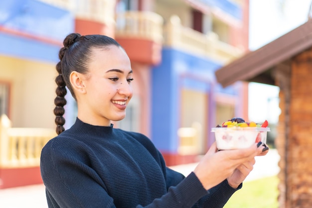 A woman is holding a bowl of fruit and smiling.