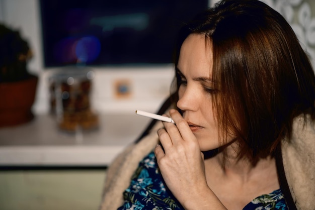 女性はタバコを手に持っている 40 歳の女性が家に座っている