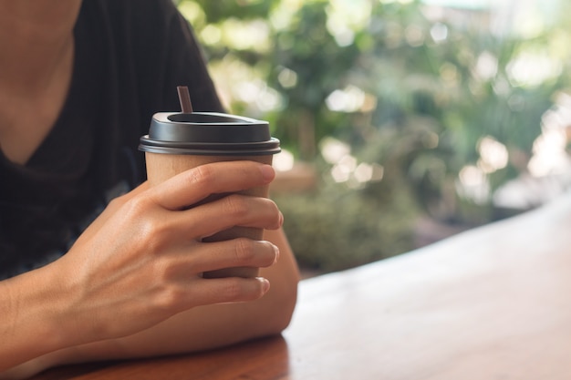 女性は正午にコーヒーショップにコーヒーカップを持っています