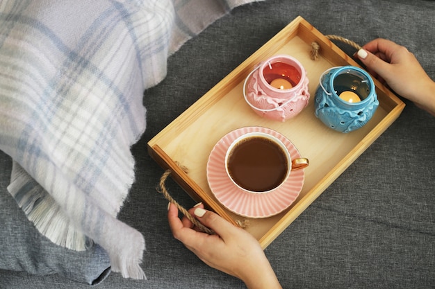 A woman is holding a cup of coffee and milk on a wooden tray 