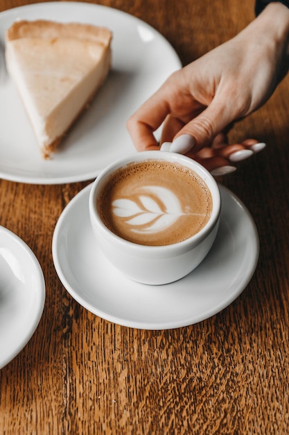 Woman is holding a cup of coffee on a wooden table near a cheesecake.