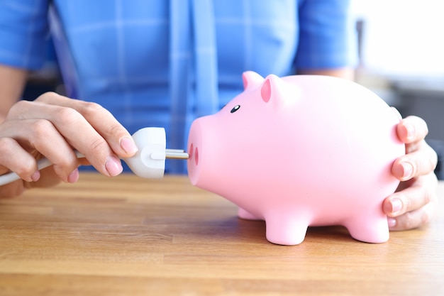 Woman is holding electrical plug and and pink piggy bank energy saving concept