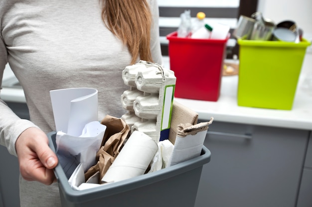 woman is holding full plastic box with assorted paper garbage