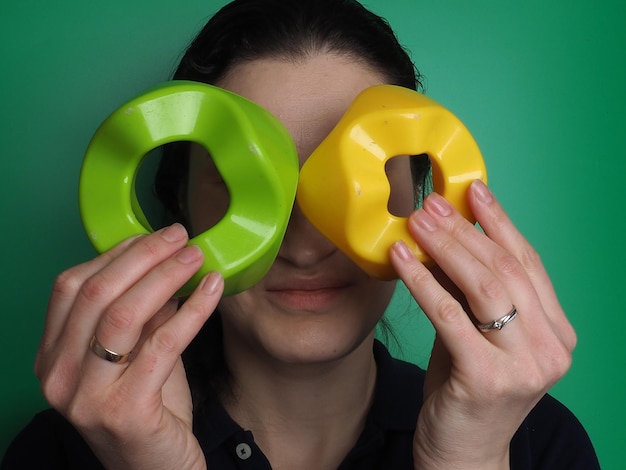 A woman is holding a green and yellow donut with the letter k on it.