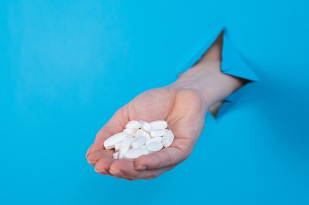 A woman is holding a handful of pills a womans hand sticks out of a hole in a cardboard blue