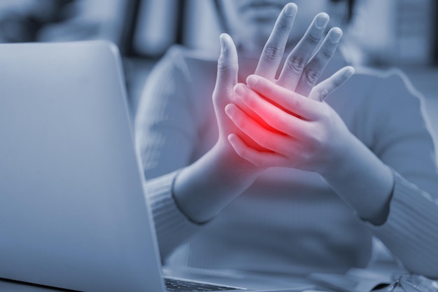 A woman is holding her hand up in pain while sitting in front of a laptop