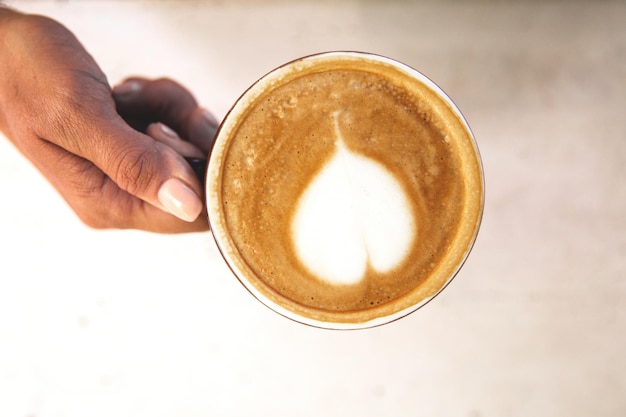 Woman is holding tasty cappucino with love art latte