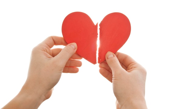 The woman is holding two parts of broken heart in her hads in front of the bright sky