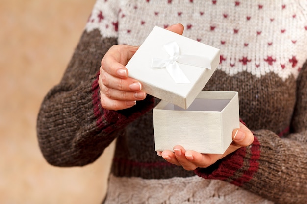 Woman is holding a white gift box in her hands and is opening it. Shallow depth of field, Selective focus on the box. Concept of giving a gift on holiday or birthday.