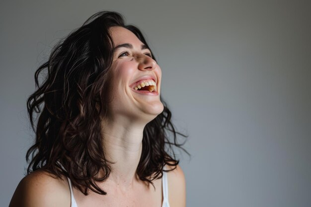 A woman is laughing and smiling in front of a gray background