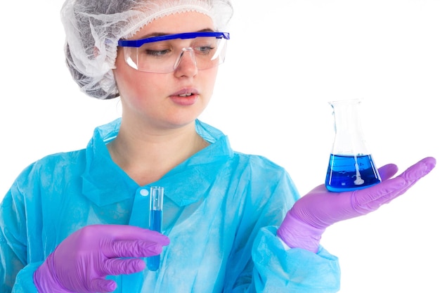The woman is looking on a flask and a tube with a blue liquid on a white background