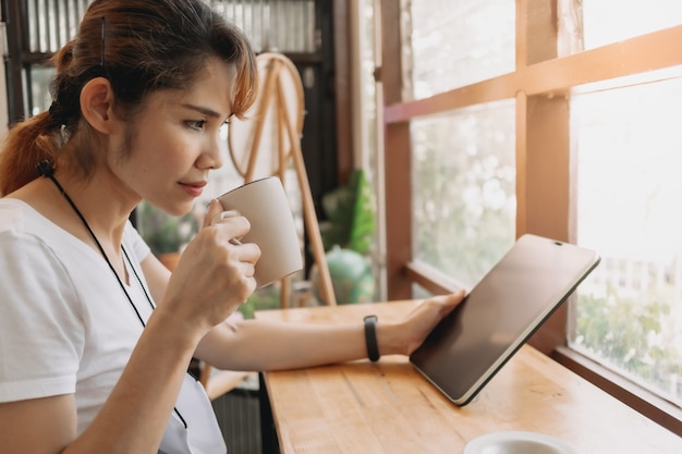 Женщина смотрит на планшет и пьет кофе в кафе