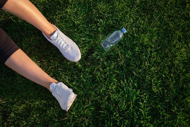 Woman is lying on the green lawn in the park. happy woman\
relaxing on the grass during sunny summer day. women\'s feet in\
white sneakers. top view. large format banner