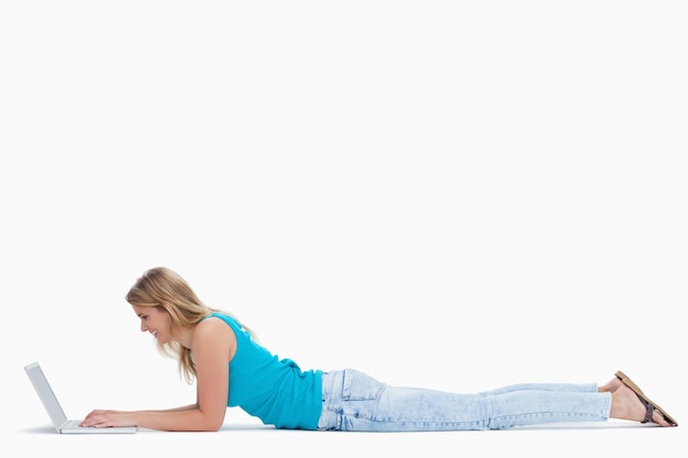 A woman is lying on the ground typing on her laptop