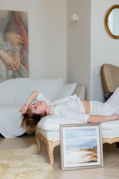 A woman is lying on a sofa in a stylish bright living room next to a beautiful picture she painted herself