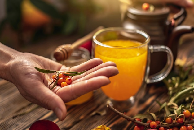 Photo woman is making a tasty and healthy vitamin tea from fresh sea buckthorn berries concept of a cozy autumn atmosphere and health care during colds and flu season