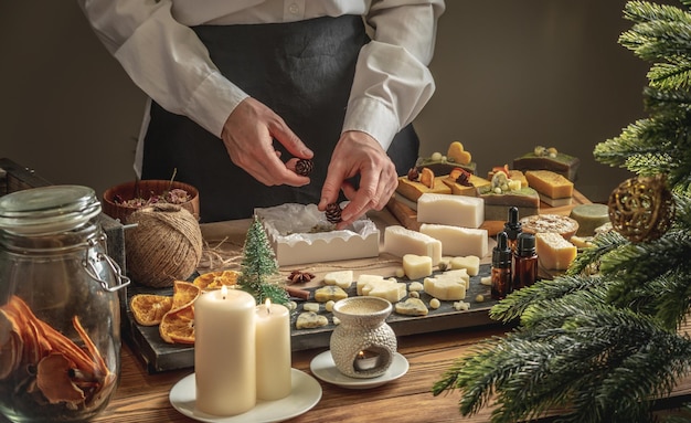 Woman is packing a beautiful natural soap into a box and decorate it with cones Process of wrapping presents for New year and Christmas festive mood handmade gifts