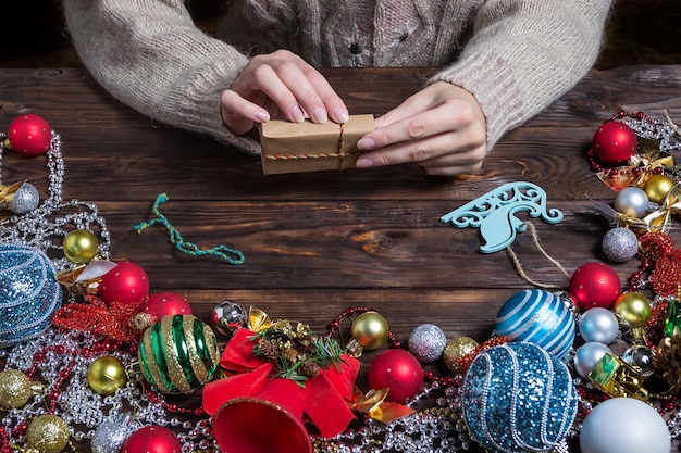 女性はクリスマスの装飾が施された暗い木製のテーブルにクリスマスプレゼントを詰めています