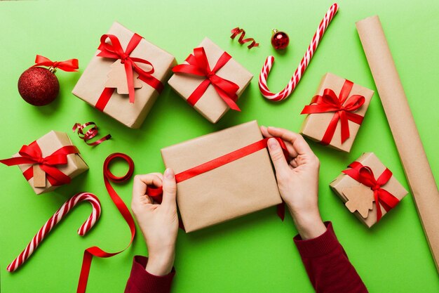 Woman is packing surprise gift for Christmas holidays sitting at workplace with craft tools top view Woman wrapping Christmas gift at colored table