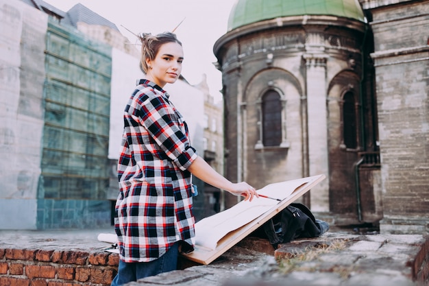 Woman is painting directly on the city street against the background of old architecture.