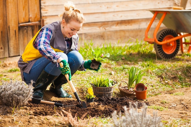 Woman is planting in the garden, gardening in spring, hands in green gloves working on flower bed