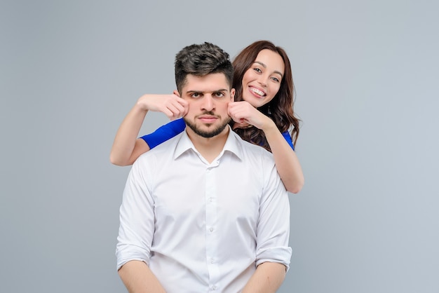 Woman is playing with her boyfriend and annoying him isolated over grey background