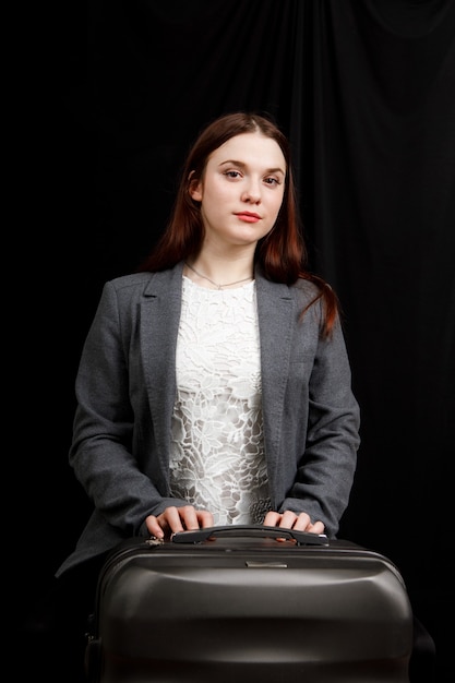 Woman is posing in a dark studio with a travel bag