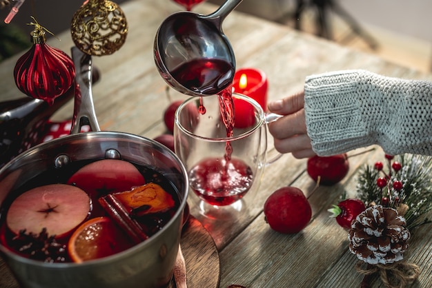 Photo woman is pouring fragrant hot spicy mulled wine into a transparent mug. concept of a cozy festive atmosphere, new year and christmas mood