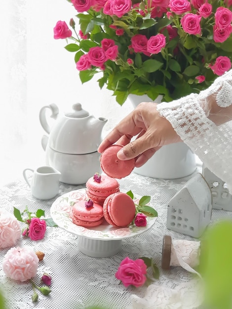 A woman is putting a pink macaroons on a plate.
