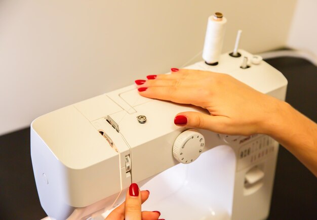 Woman is putting thread in sewing machine Fashion concept Freelance work at home Creating of new clothes process Hobby ideas