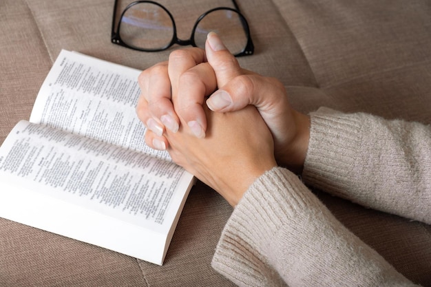 Woman is reading the Holy Bible and praying on sofa in room