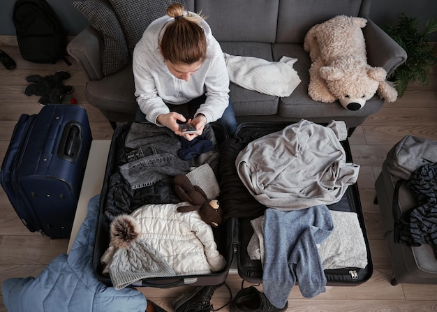 Foto una donna è pronta per uscire di casa e fare le valigie. la donna guarda nel telefono