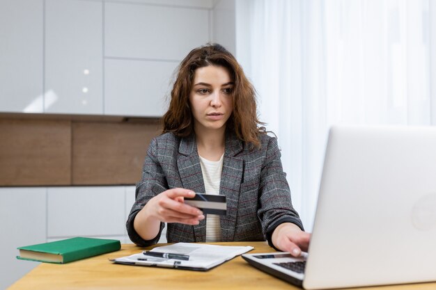 The woman is relaxing at home, shopping online, using a laptop and a credit card