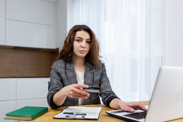 The woman is relaxing at home, shopping online, using a laptop and a credit card