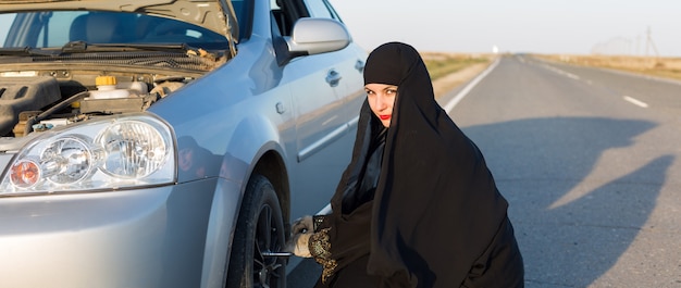 Woman is replacing a punctured car wheel.