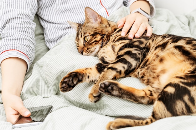 女性はベッドで休んでいて、ペットの猫は彼女の腕の中で眠っています。