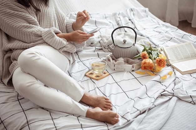 A woman is resting in bed with tea, a book and a bouquet of tulips. Spring morning and weekend concept.