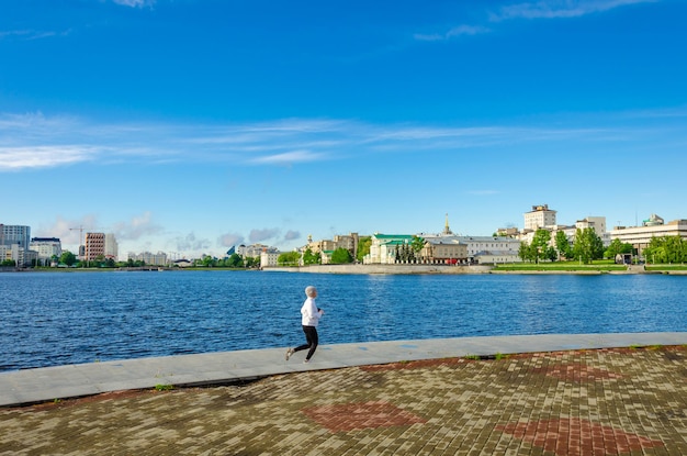 A woman is running on the embankment near the river