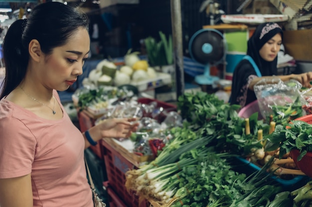 女性はタイの地元の新鮮な市場で買い物をしています。