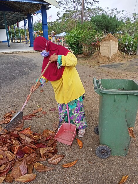 A woman is shoveling leaves with a red cloth on at the garden