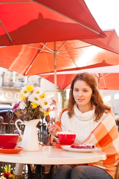 Женщина сидит в кафе на открытом воздухе и ест торт и какао, уютная осень