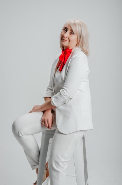 a woman is sitting on a chair in a white suit with a red scarf