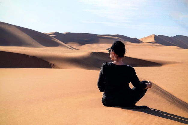 A woman is sitting on the golden sand dune of the Namib desert Africa