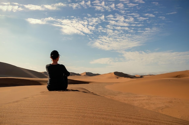 A woman is sitting on the golden sand dune of the Namib desert Africa