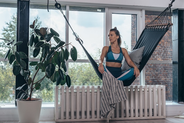 Woman is sitting at home in a hammock and resting.