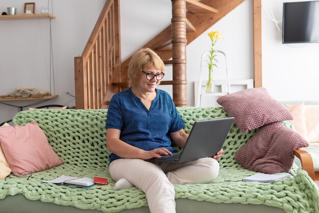 A woman is sitting in a room on a sofa with a laptop