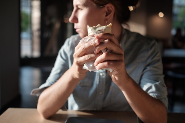Foto la donna è seduta in un piccolo caffè e tiene in mano un involucro di tortilla prima di mangiare guardando da parte
