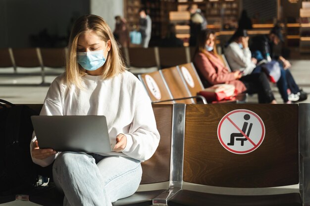 Foto la donna è seduta nella sala d'attesa con un portatile in maschera medica