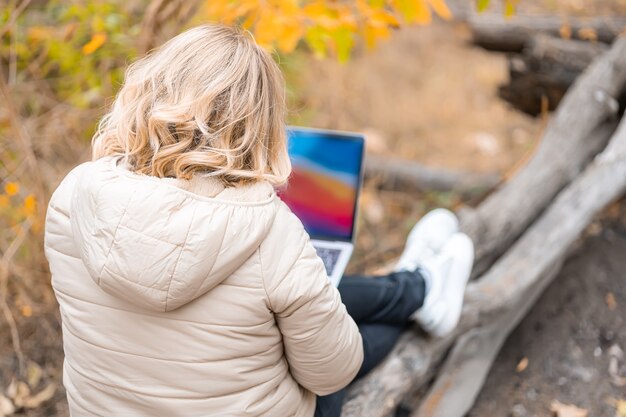 A woman is sitting with her back and working at a laptop in an autumn park